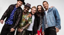 Banda Backstreet Boys posa para foto em fundo branco e com roupas coloridas, rindo e se abraçando