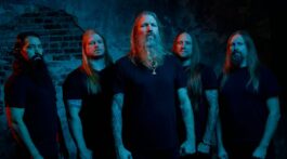 Banda Amon Amarth posa para foto em frente a muro destruido e com luzes vermelhas e azuis