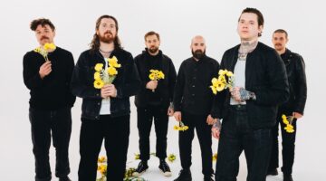 Banda The Devil Wears Prada vestida de preto, segurando flores amarelas em fundo branco